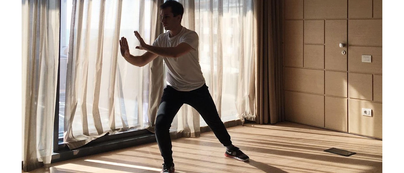 Man in a vest and tracksuit bottoms practices Tai Chi in an airy studio