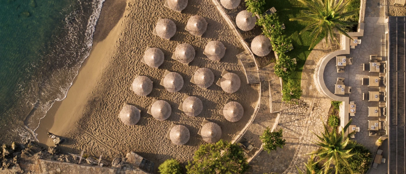 Sandy cove lapped by waves, lined with thatched parasols and loungers
