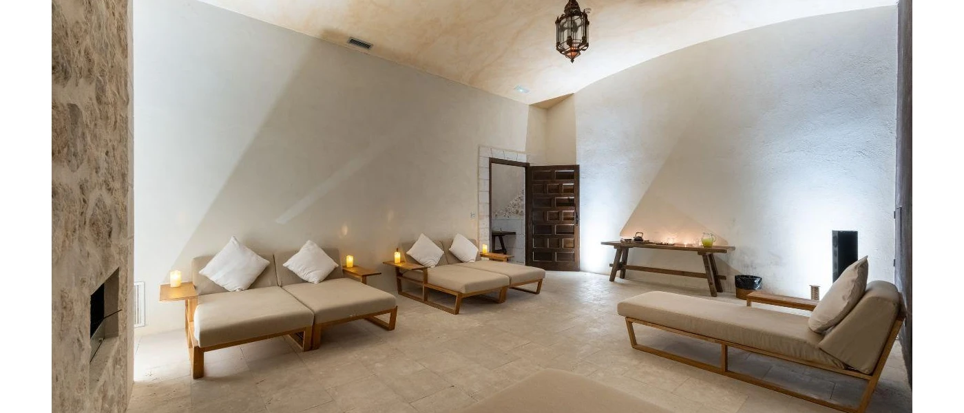 Neutral coloured room with a black lantern-type ceiling light, wooden cushioned chairs and tables with lit candles