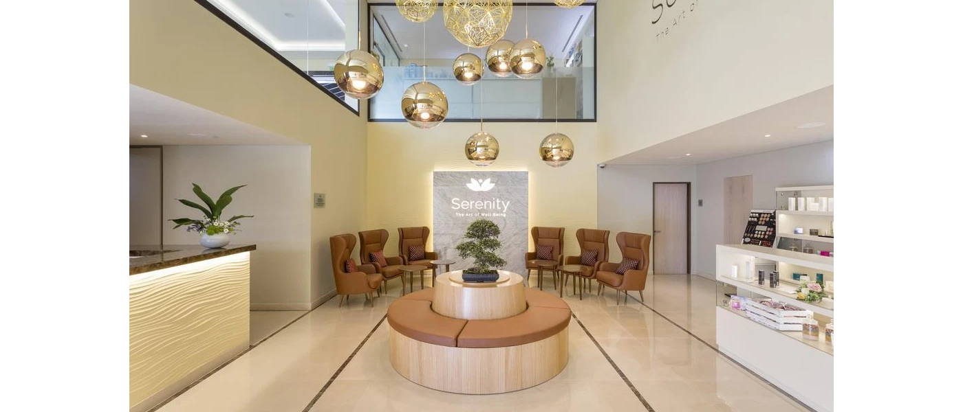 Spa entrance area with a cluster of gold pendant lights, a circular sofa with brown leather and matching armchairs, a large desk and a shelf of cosmetic products