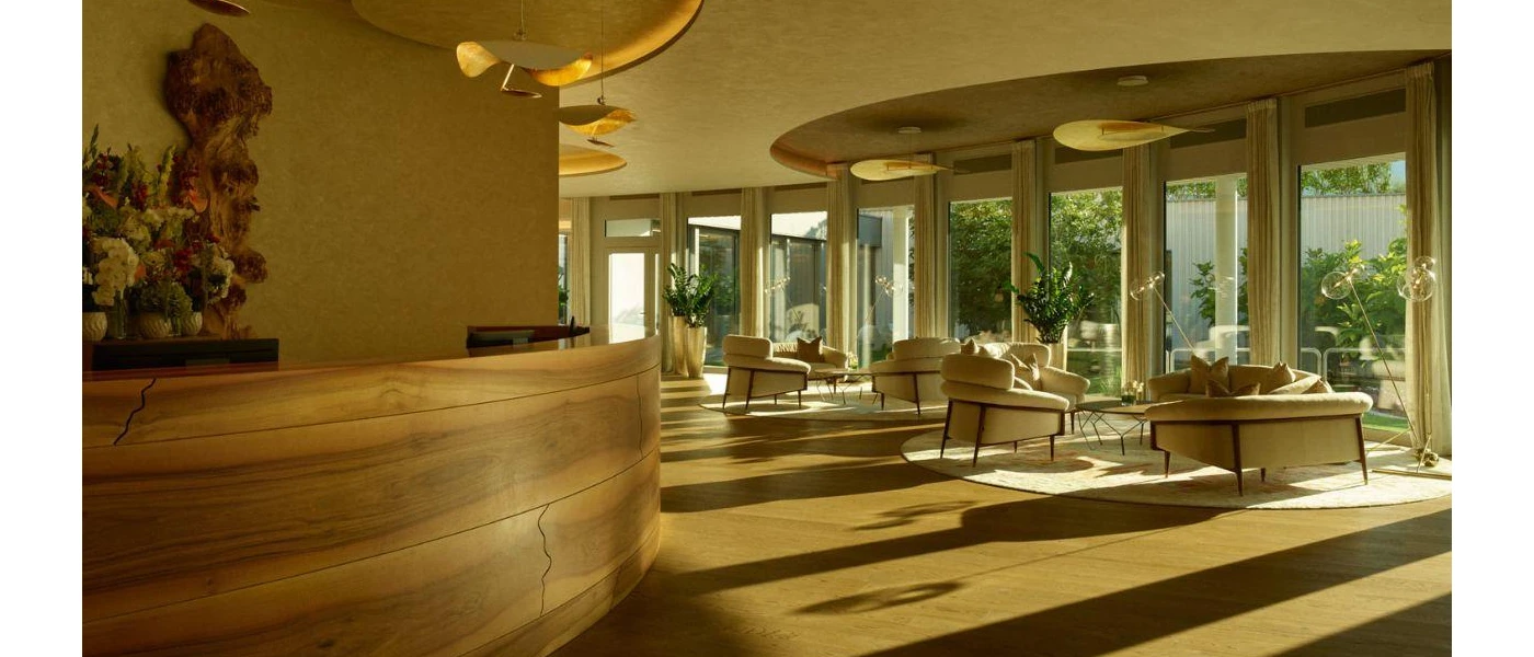 Sunny room with full-length windows, a sleek wooden reception desk, neutral armchairs and potted plants