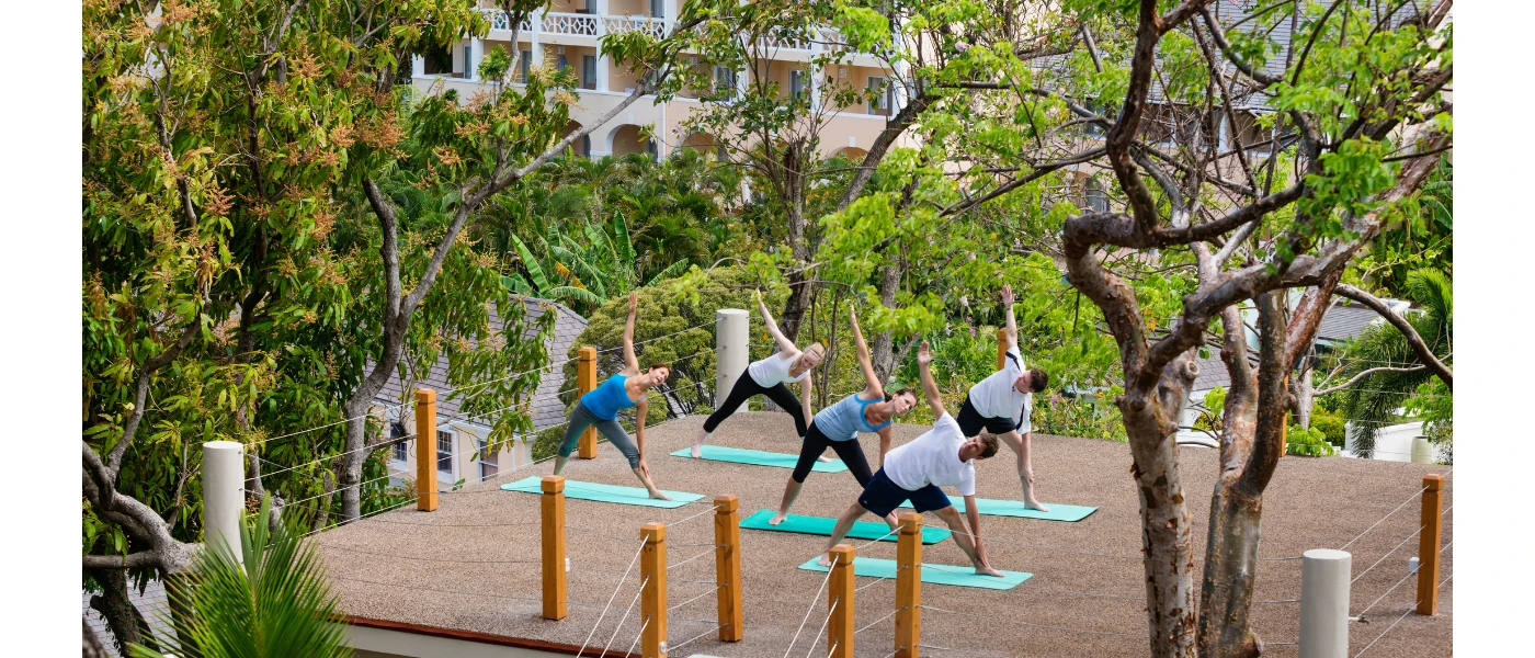 Group practice yoga on green mats on in a courtyard surrounded by greenery