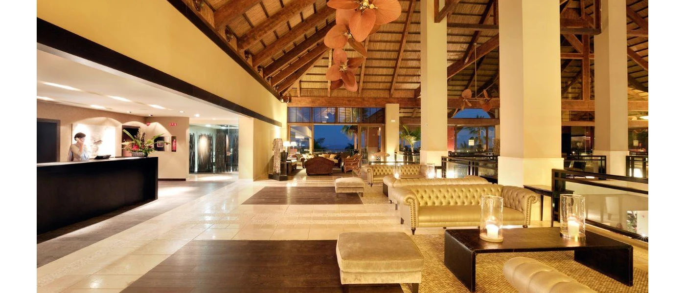 Warmly lit lobby area with large pillars, pink flower-shaped lights, wooden beamed ceilings, chesterfield-style sofas and a large dark-wood reception desk
