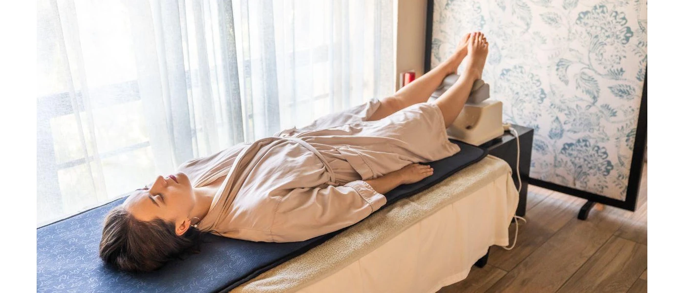 Woman in a beige robe lying on a massage bed with her feet up on a machine