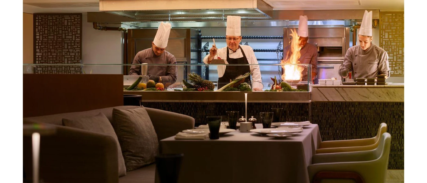 Chefs hard at work at a live cooking station as seen from the restaurant dressed in neutral colours
