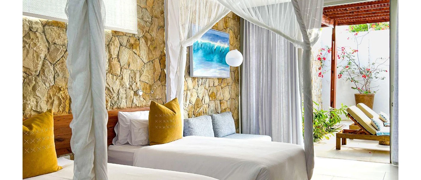Cobbled stone wall with white twin beds and mustard cushions overlooking a furnished terrace