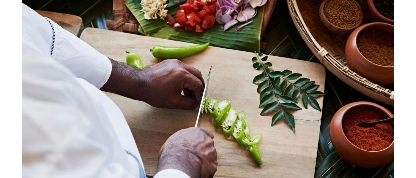 Chef in whites chopping up vegetables on a wooden chopping board surrounded by pots of spices