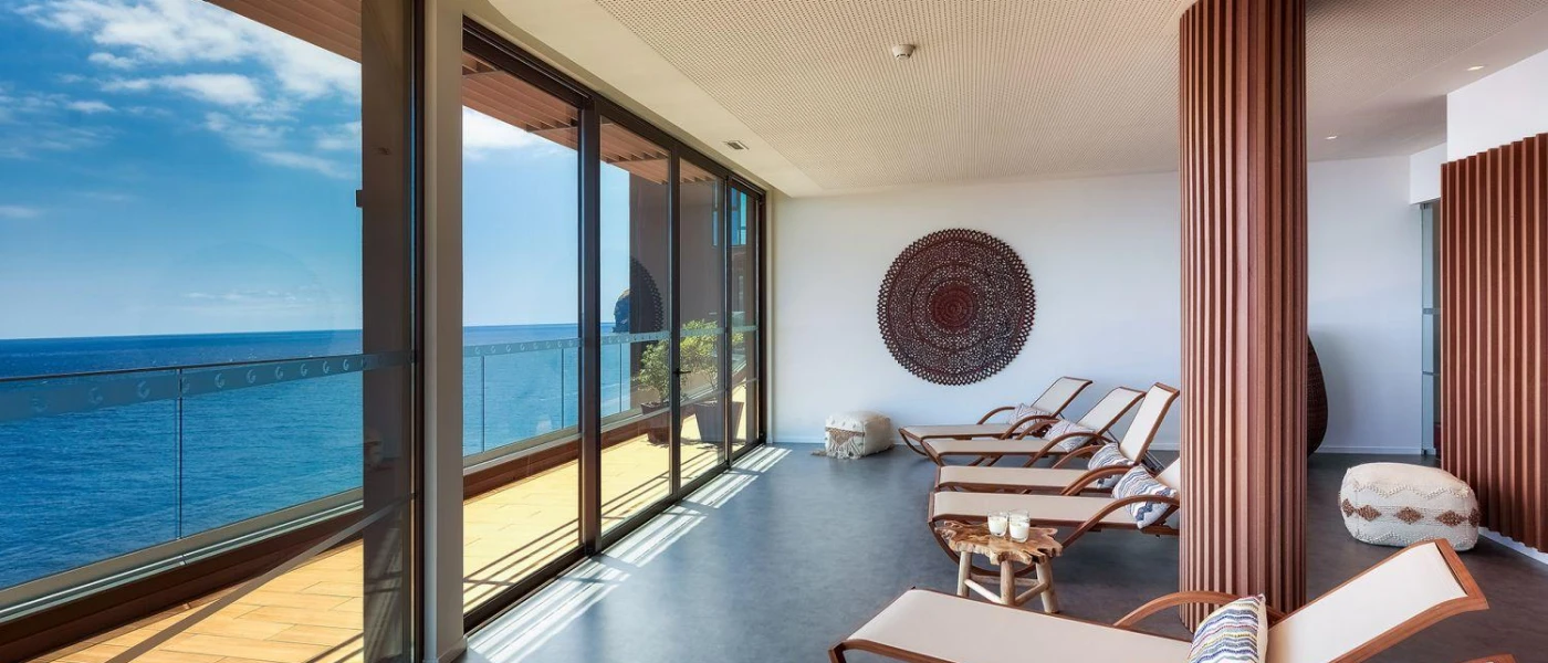 Loungers lined up in a sea-facing room with full-length windows overlooking a sea-facing balcony