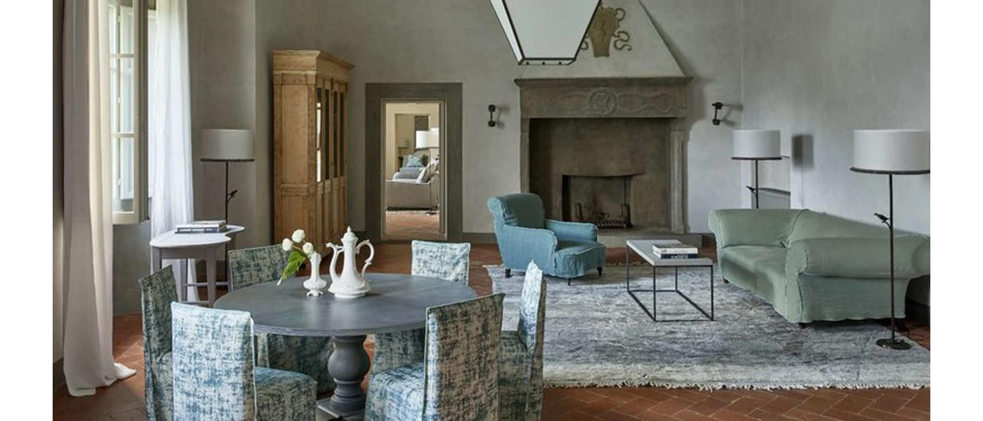 Elegant hotel room with a blue and white patterned rug and chairs, white walls and a grand stone fireplace