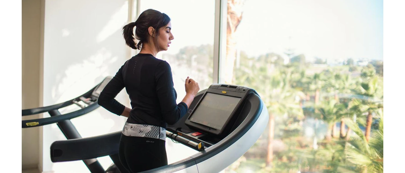 Woman in black active wear running on a treadmill in front of a window overlooking tropical greenery