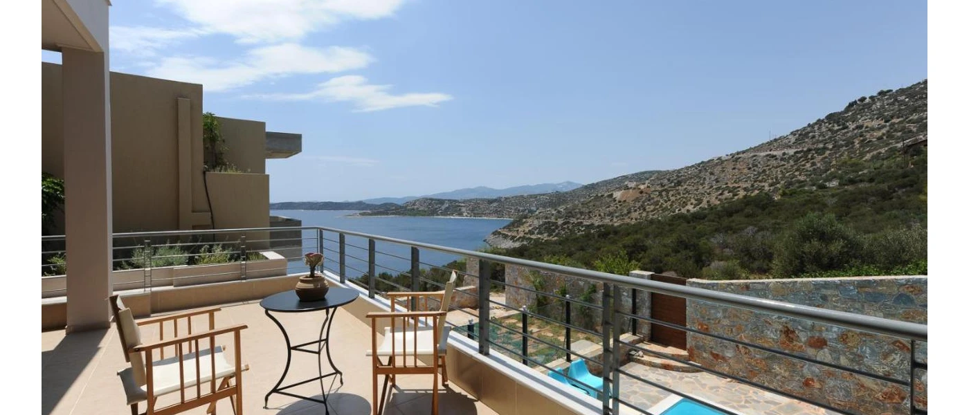 Furnished terrace overlooking the stone walls and swimming pool below, and the hills and Aegean Sea in the background