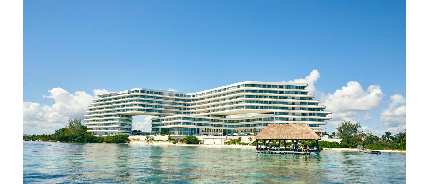 High-rise, multi-storey white resort on a white-sand beach overlooking the sea, under a blue sky with white clouds