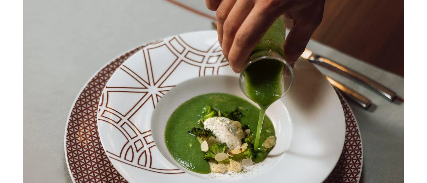 White plate with rice and broccoli in a green sauce, as a staff members pours more on