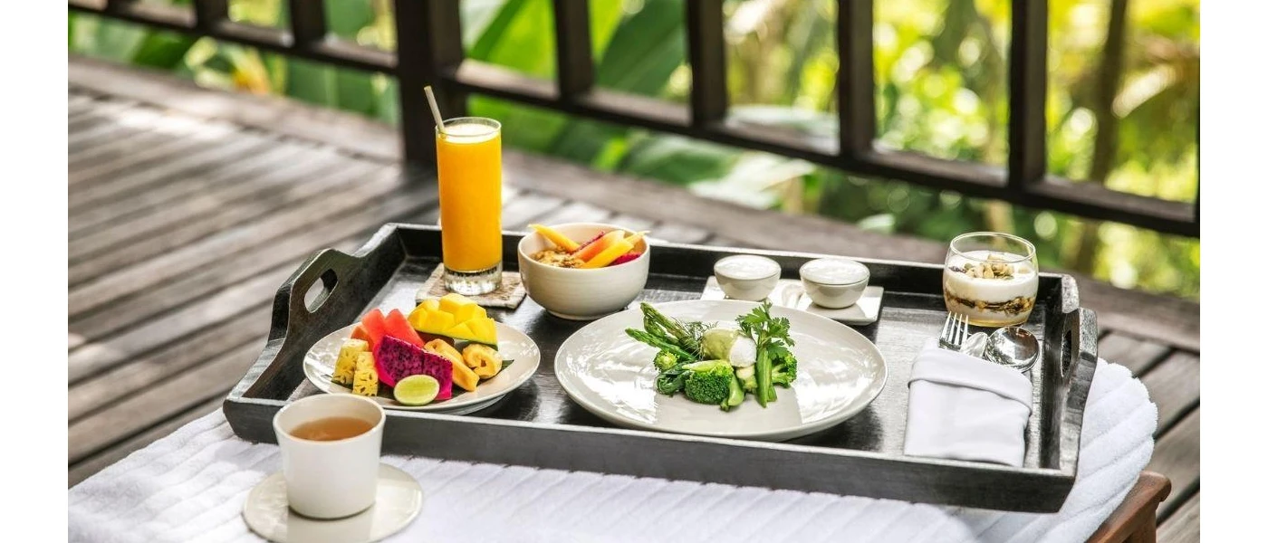 Tray with orange juice, a plate of fruit, a plate of green vegetables and a cup of herbal tea