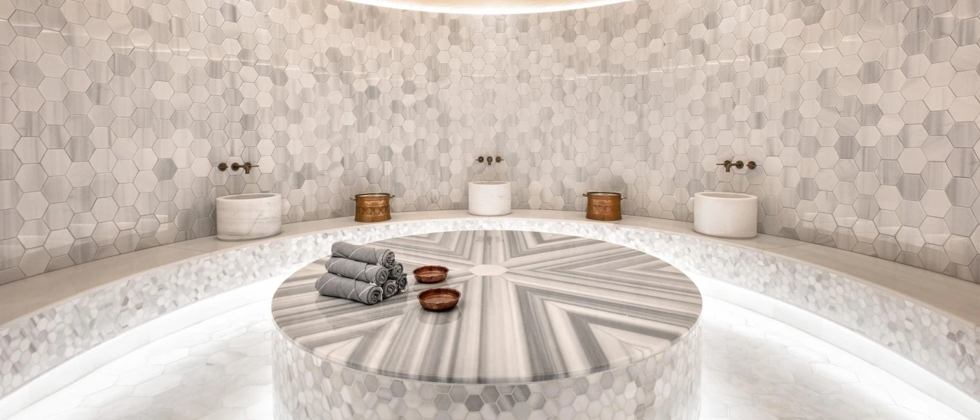 Marble, grey-tiled spa room, with sinks, towels and surrounding benches