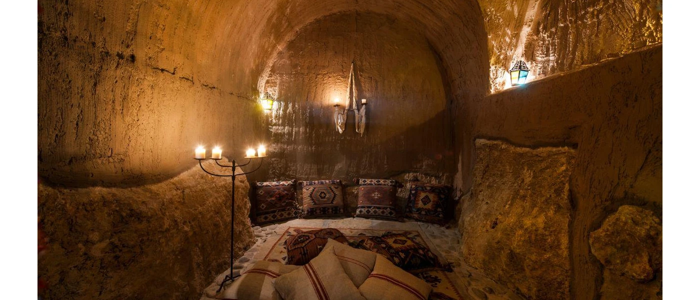 Stone cave with patterned carpet and cushions lit by candlelight 