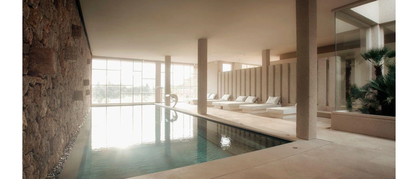 Indoor swimming pool next to a stone wall with white loungers opposite