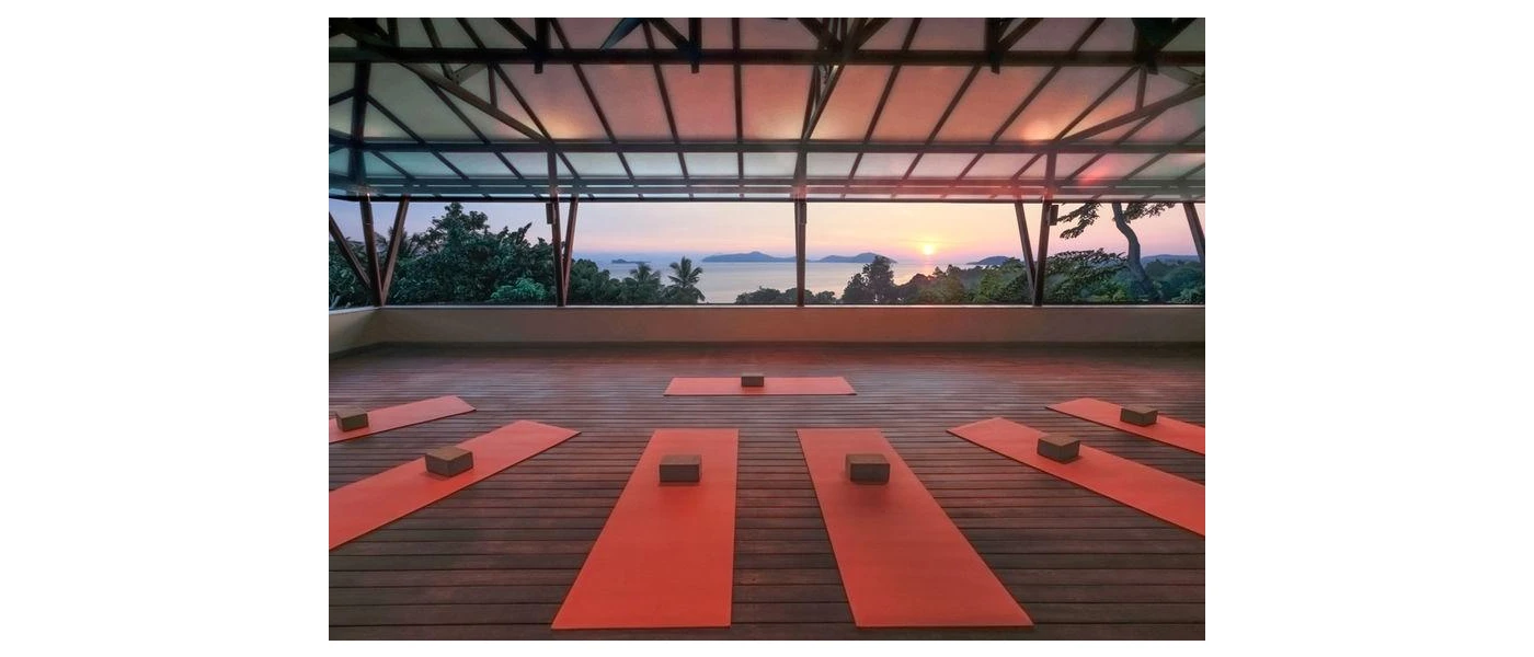 An open-air pavilion with an ocean view set up for a class with red and brown yoga mats and blocks