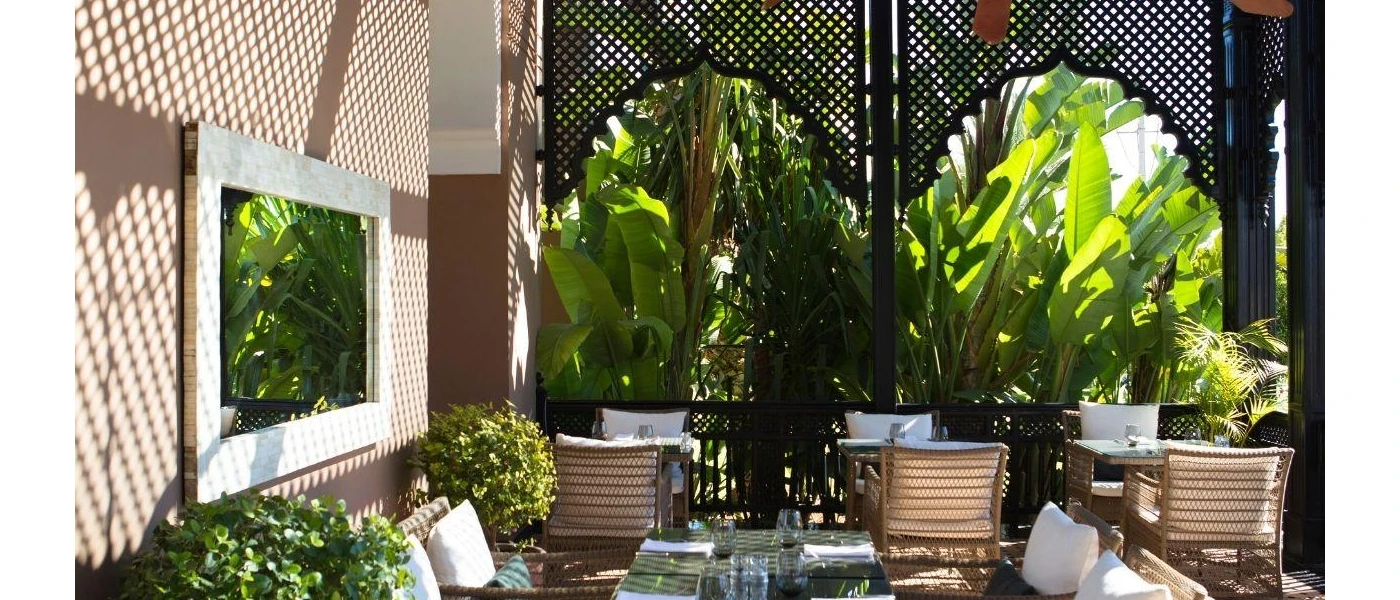 Outdoor tables and chairs next to tropical greenery and a white mirror hanging on the wall