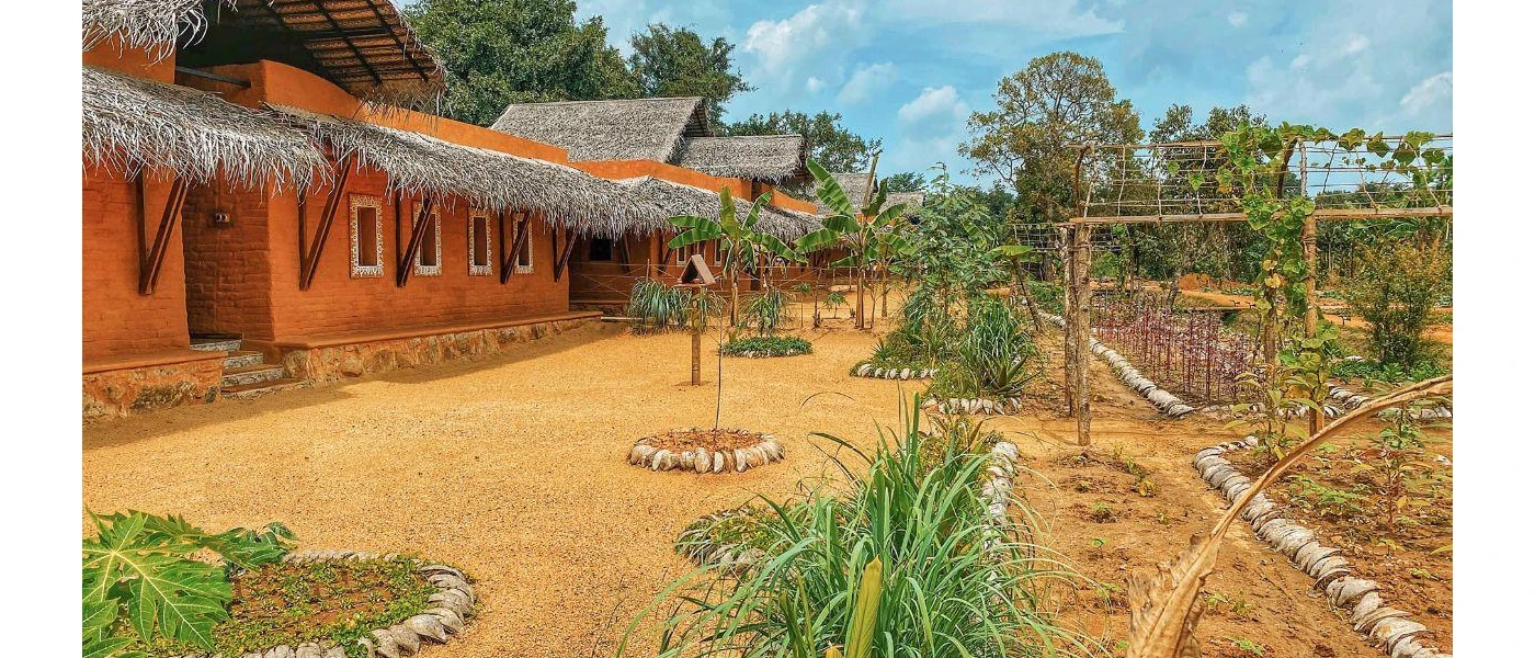 Low-rise orange building with a thatched roof, next to a kitchen garden under a blue sky