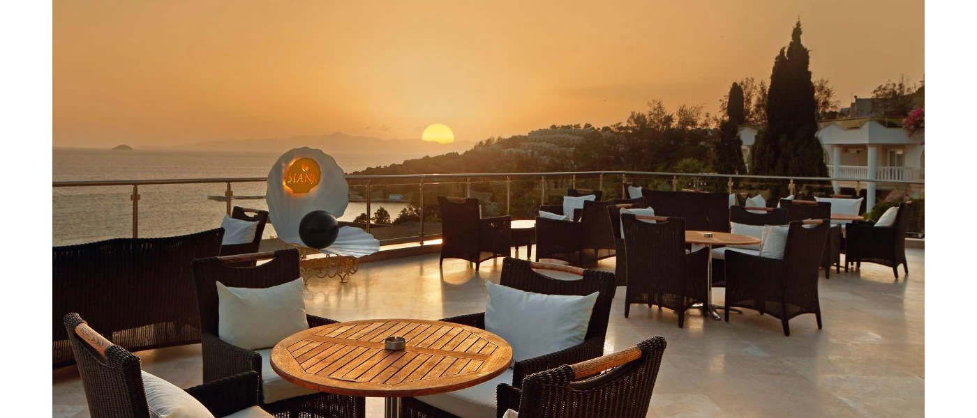 Rooftop sea-facing terrace at sunset, with black rattan chairs and wooden tables, and a giant oyster sculpture with a black pearl and the word 'Sianji' written in gold