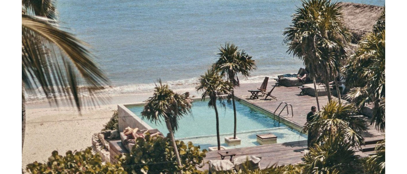 Tall palm trees huddle around a swimming pool overlooking a white-sand beach and the sea