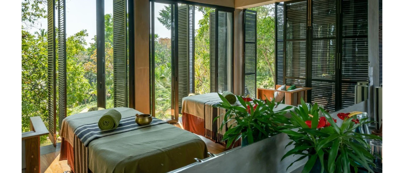 Large spa treatment cabin open to the elements, with wooden shutters, two massage beds, sound bowls and plants