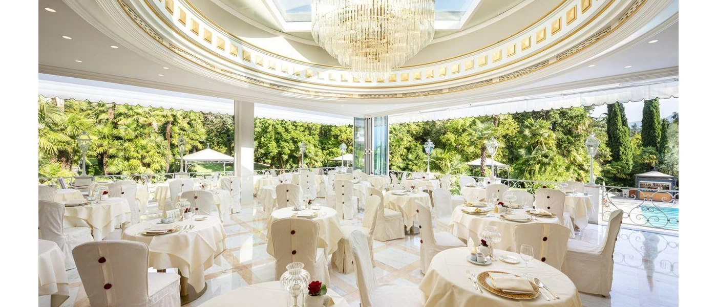 Elegant open-sided restaurant with a domed ceiling, glittering chandelier, white chintzy tablecloths and surrounding gardens