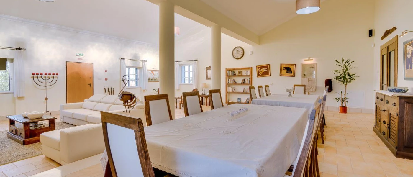 Long communal table with a white tablecloth in a neutral dining room