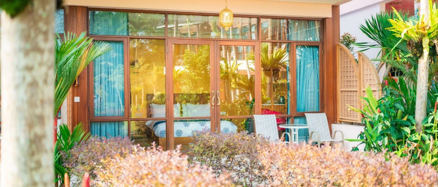Balcony with a table and chairs, overlooked by a hotel room with blue curtains and a mustard colour wall