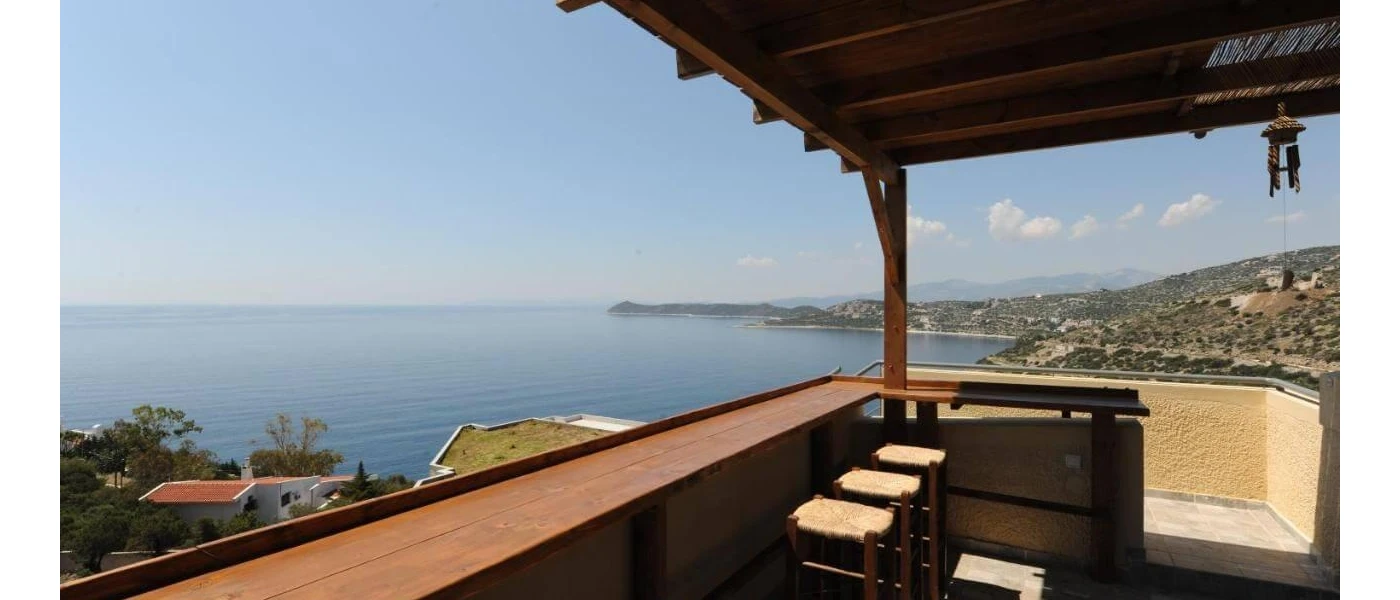 Thatched-roof open-sided terrace with wooden stalls and a sweeping Aegean Sea view