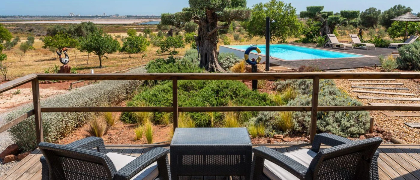 Wooden balcony with chairs and a small table, overlooking the swimming pool and gardens