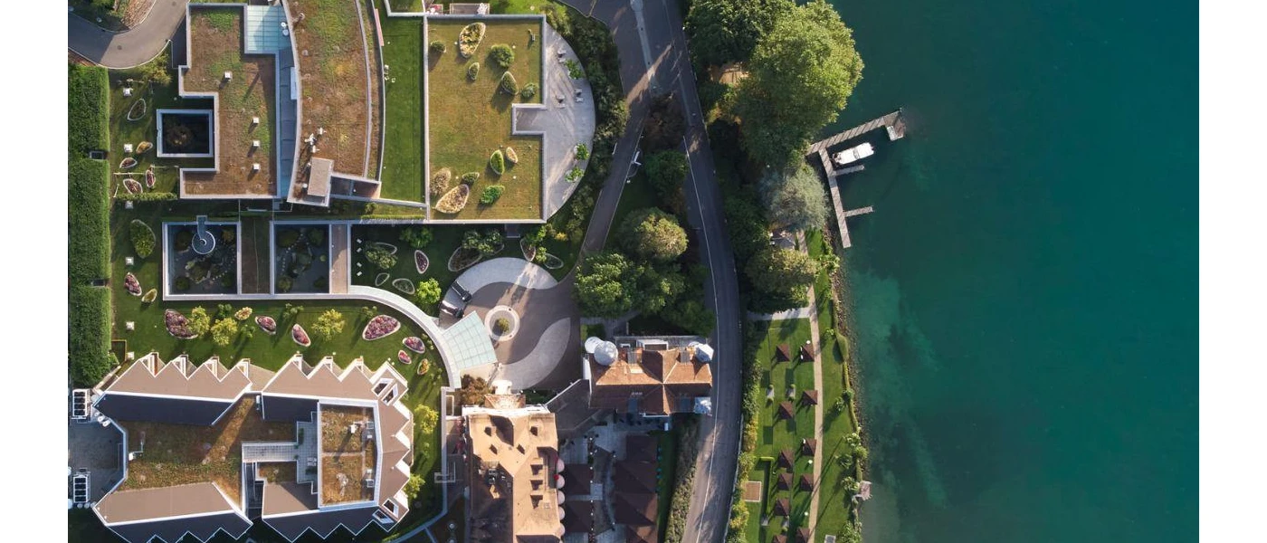 Landscaped grounds next to an inky blue lake fringed by greenery, shot from above