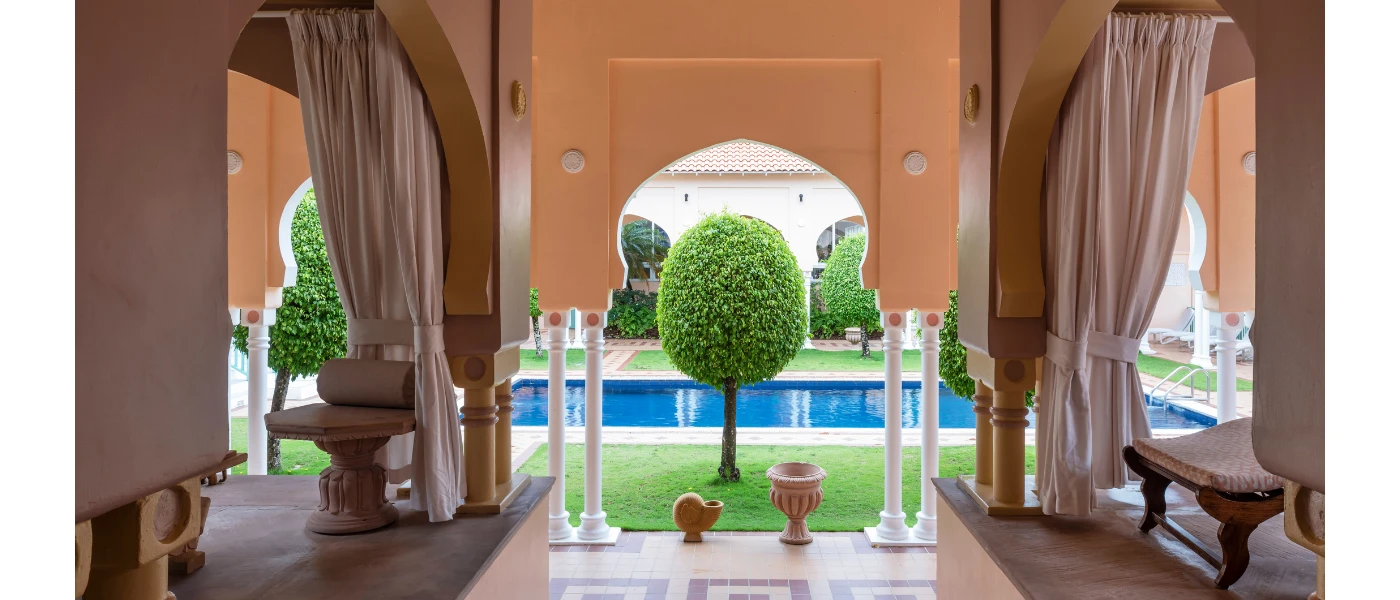 Relaxing area with terracotta walls and white curtains overlooking a swimming pool surrounded by trees