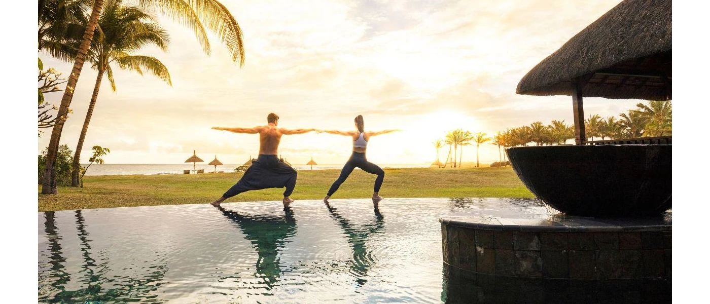 A man and woman with knees bent and arms outstretched next to a water feature overlooking the ocean