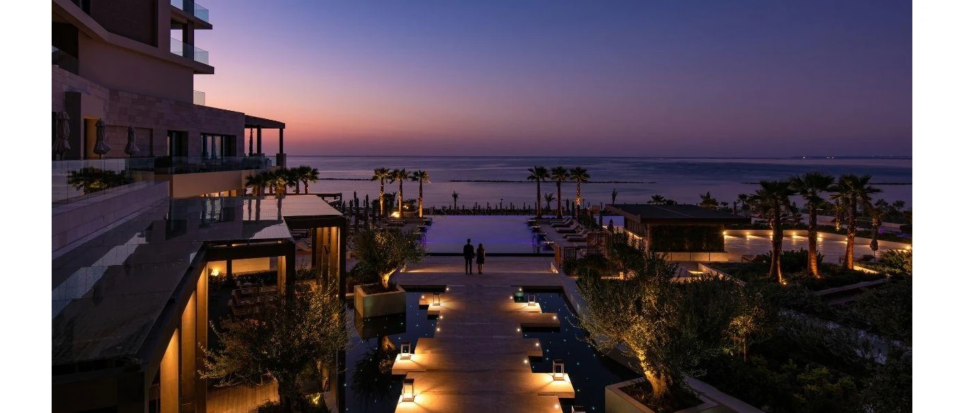 A lantern-lit wooden jetty leading to an infinity pool and view of the sun setting over the ocean