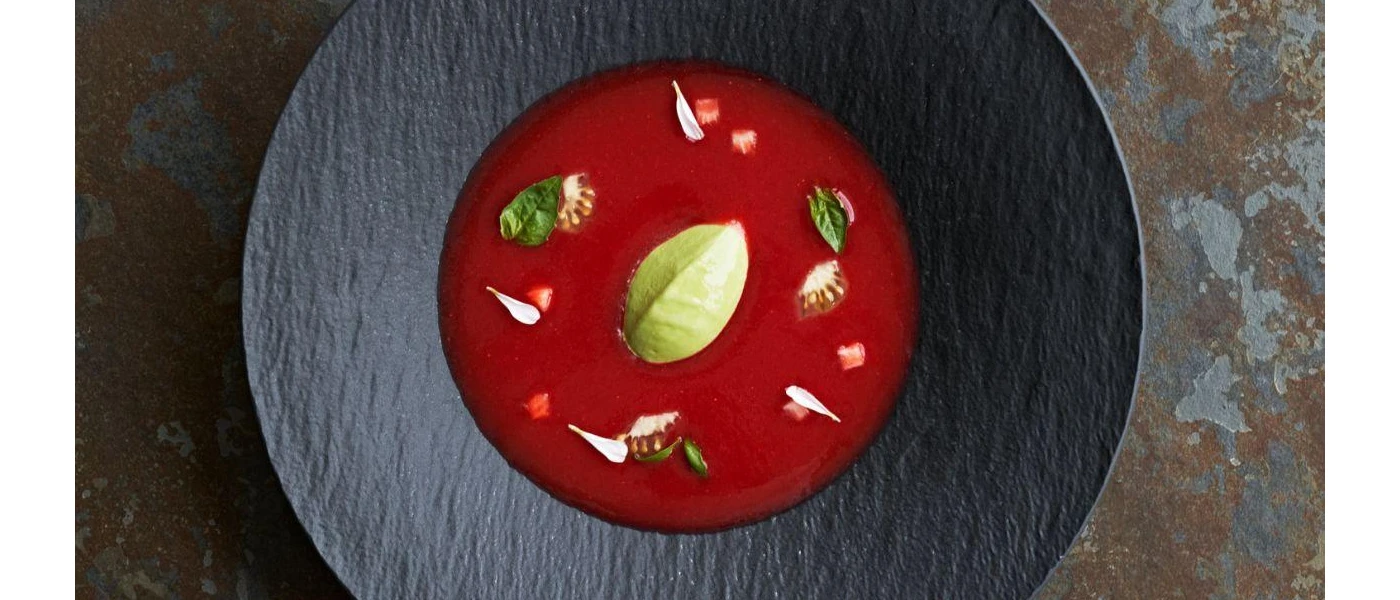 Dark grey bowl with a red think liquid inside, garnished with green leaf-like vegetables