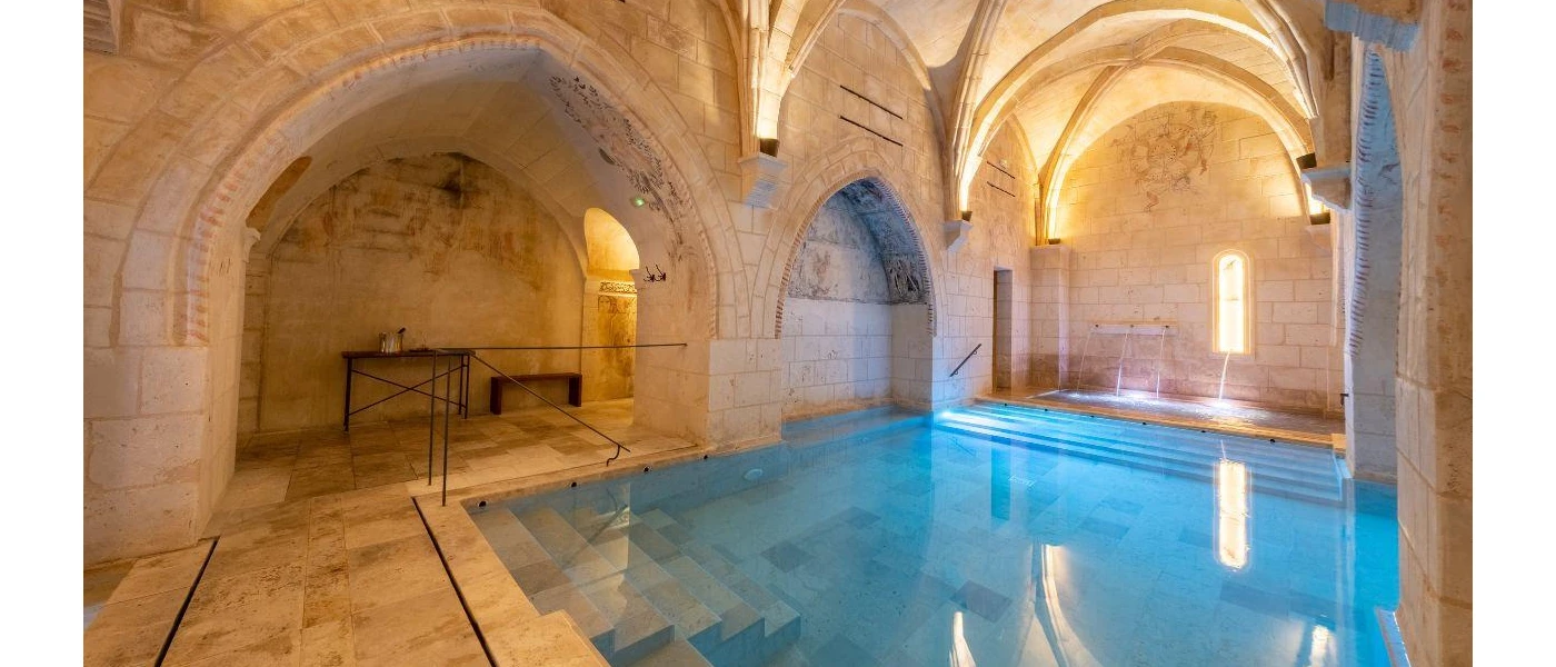 Indoor pool in a warmly lit vaulted room with a stone floor, stone walls and a stone ceiling