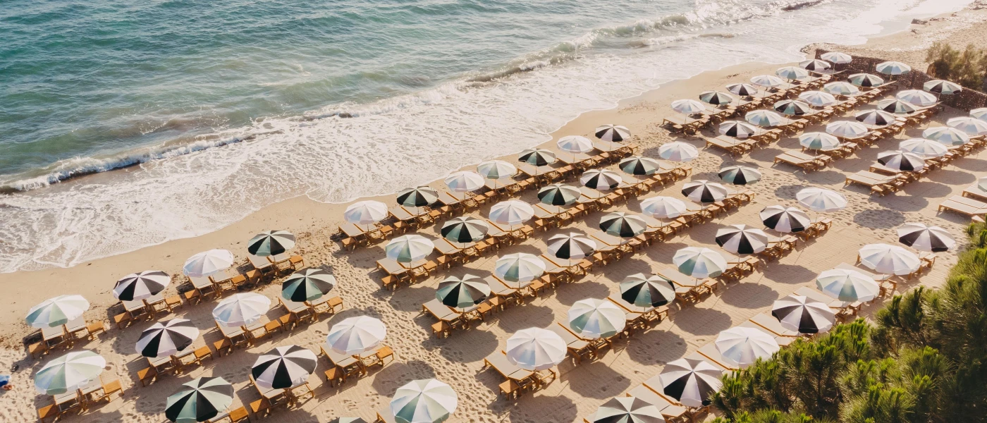 Sandy beach lined with striped parasols and wooden loungers, washed by gentle waves