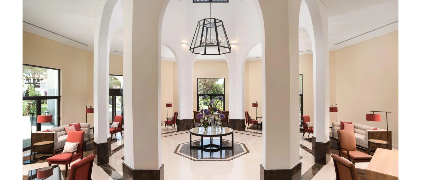 Airy lobby area with cream walls and white pillars, a black pendant light, terracotta chairs and cream sofas