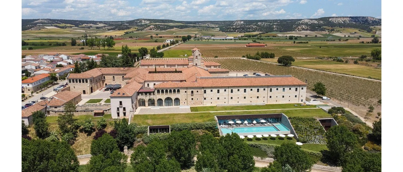 Terracotta-roofed, sand-coloured monastery with a swimming pool, surrounded by greenery and vineyards