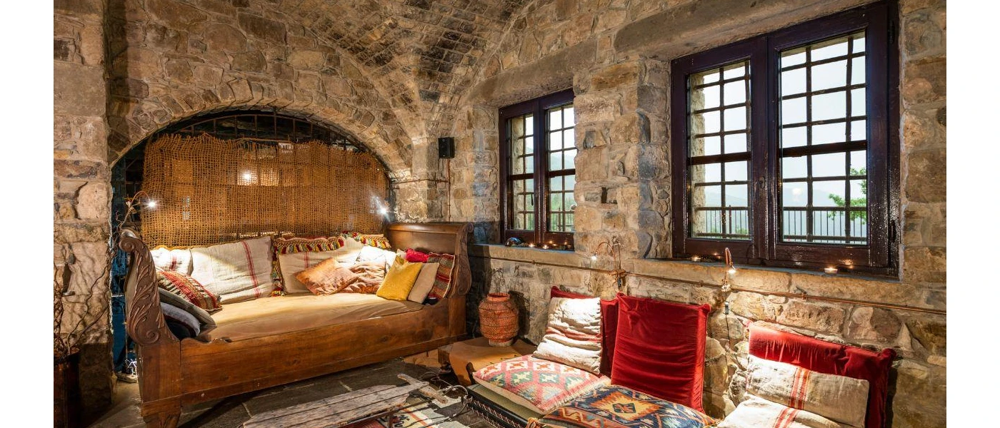 Cosy, patterned low-level chairs and cushions in a room with stone walls and a stone ceiling and dark-wood windows