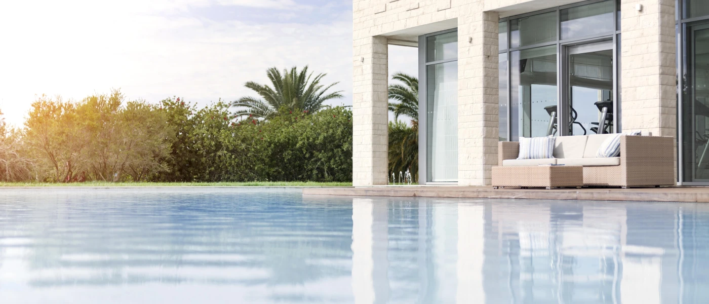 Stone building behind a grey cushioned sofa, overlooking a swimming pool and a band of greenery