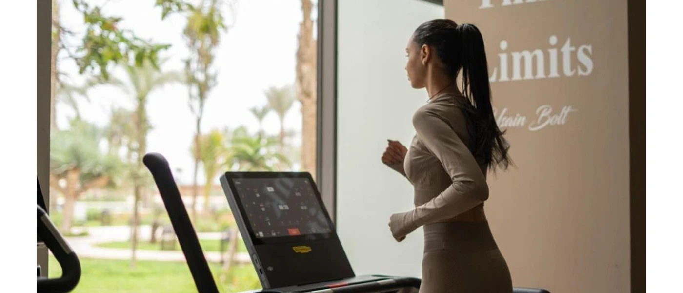 Woman in active wear running on a treadmill in front of a window overlooking tropical gardens