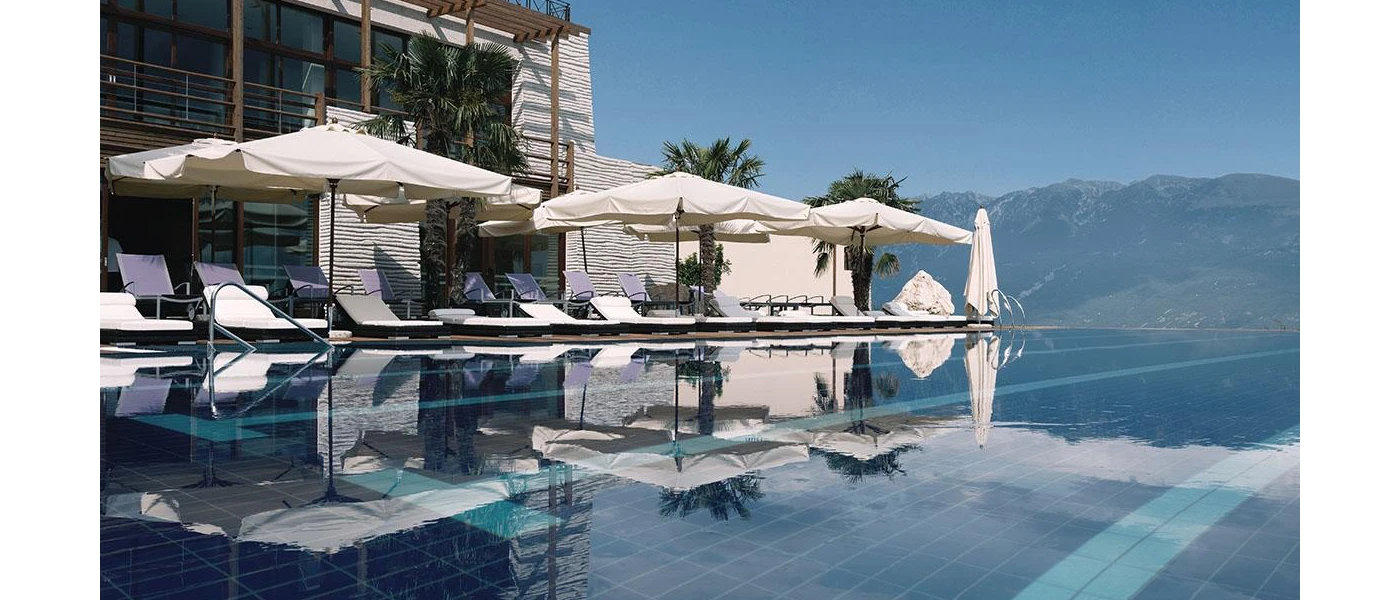 Infinity pool lined with ivory cushioned loungers and parasols, with mountain peaks in the background