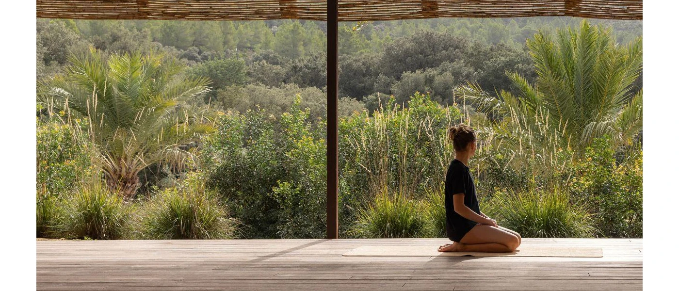 Woman sitting on her knees next to a window overlooking lush vegetation