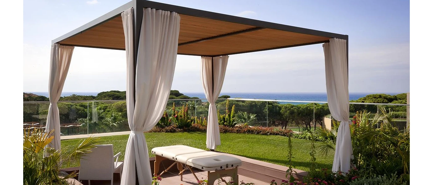 Outdoor treatment bed under a four-poster cabana, surrounded by a garden and with a sea view