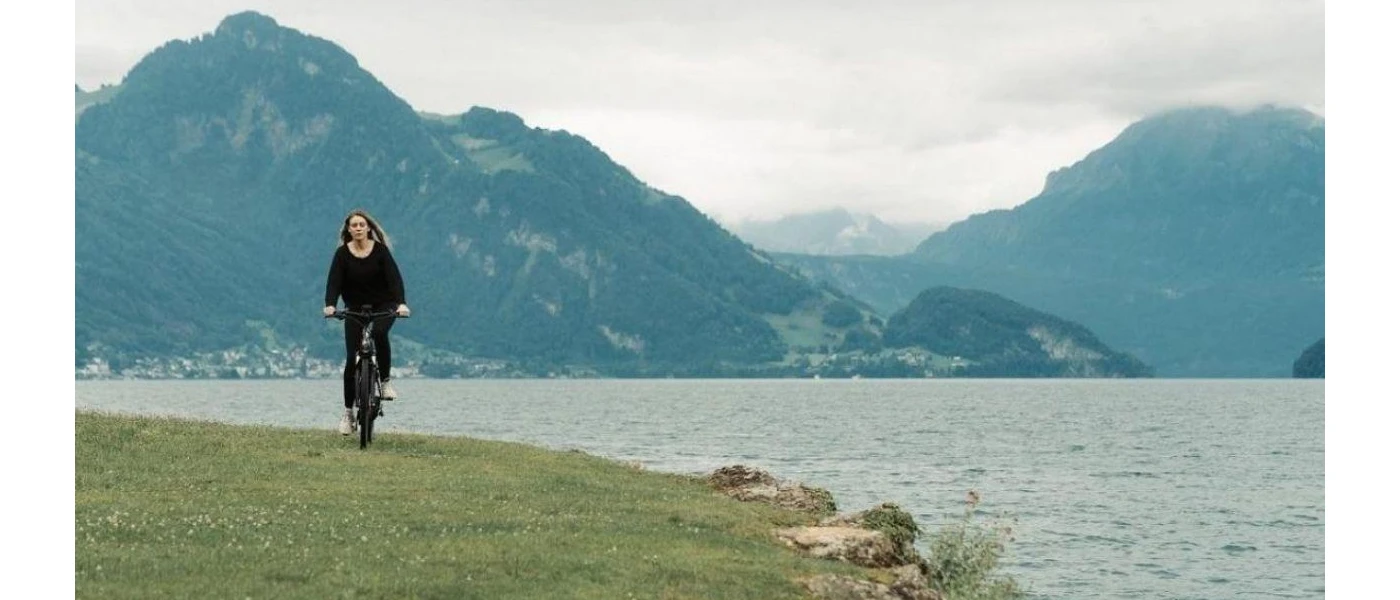 Woman in black cycling along a grassy bank on a lakeside