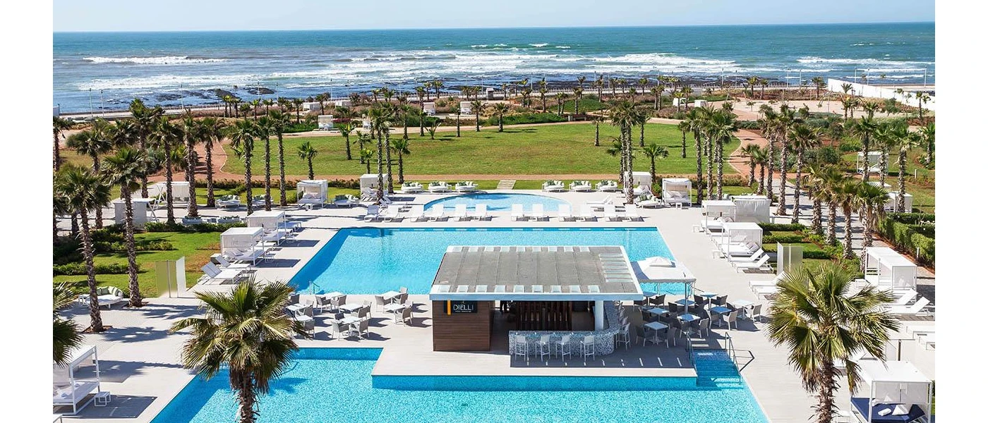 Sunny terrace with large rectangular swimming pool with a bar in the middle and surrounding lawns and palm trees