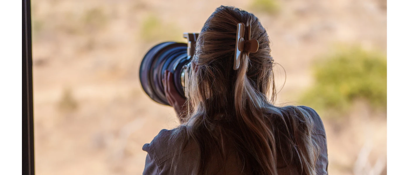 Woman with long hair in a clip takes pictures with a large professional camera in the African wilderness